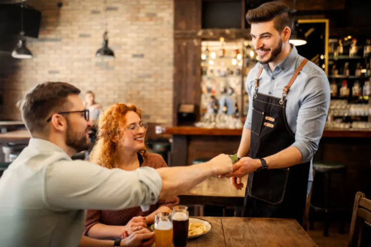 Smiling American waiter receiving a tip at a restaurant.