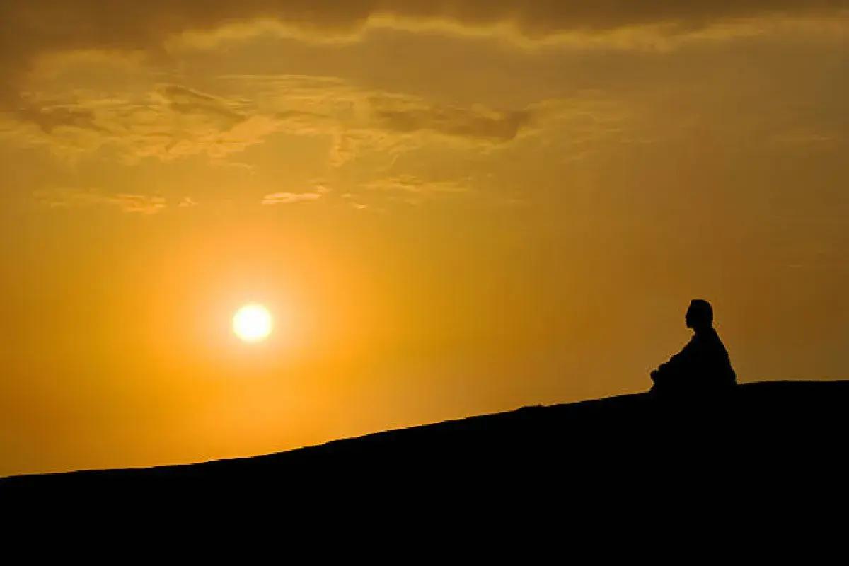 A person reflecting on a hilltop at sunset, overlooking a vast horizon