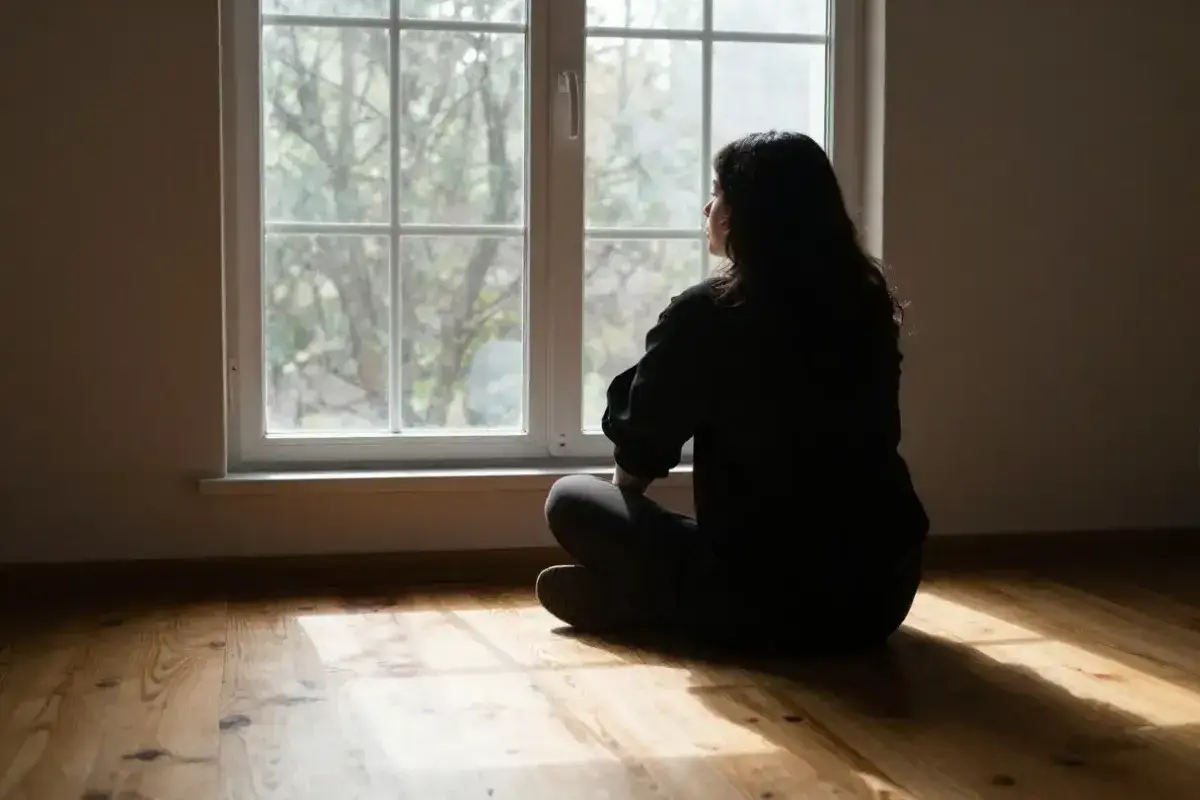  A single figure sitting by a window looking outside, light coming in