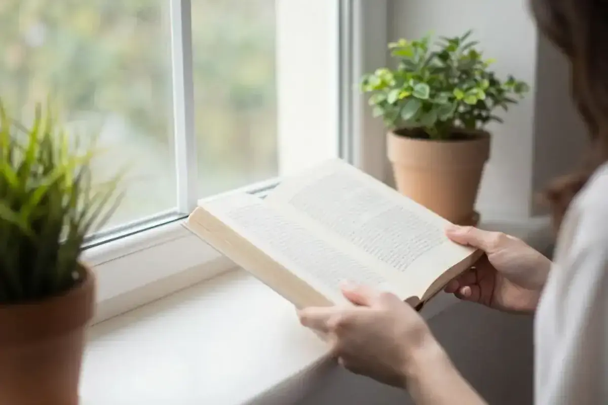 Person reading a physical book near a window with natural light