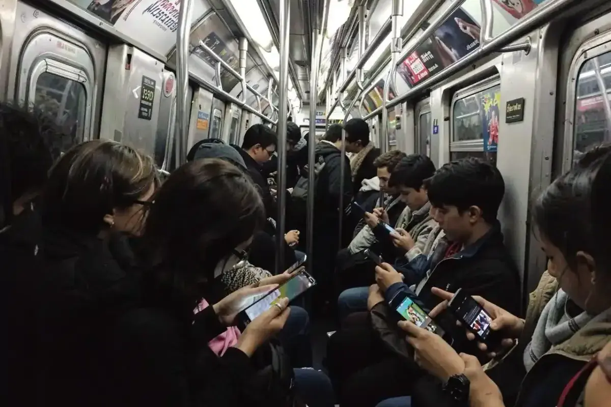 Busy subway train where several passengers without earphones are using phones with different media playing.
