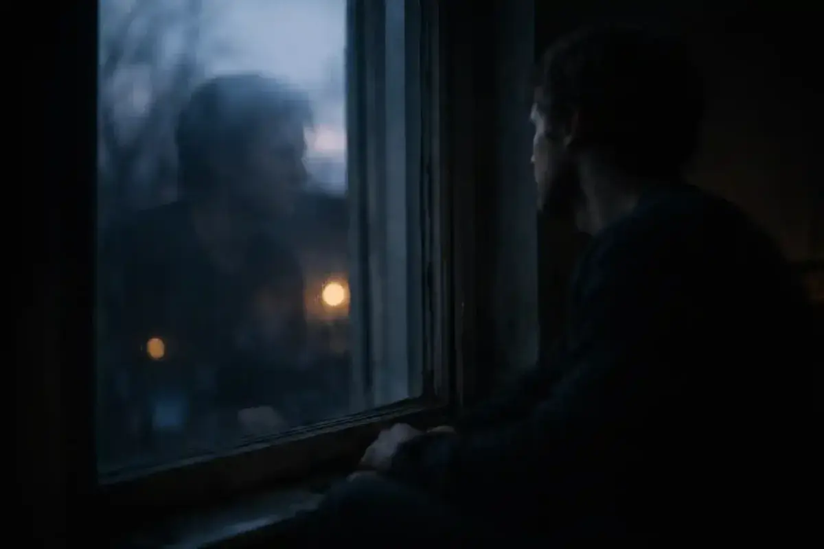 A man sitting alone near a window at night thinking deeply