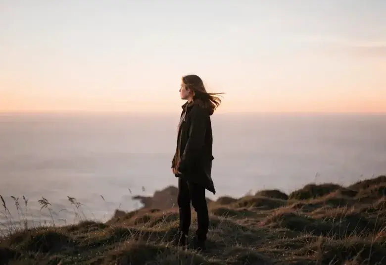 Lone figure standing on a windswept hill at dusk, contemplating in the quiet light