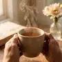 Close-up of hands holding a warm ceramic mug of tea, with a book and soft sunlight in the background, symbolizing the peace and sufficiency of simple, intentional moments
