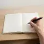 Hands holding a pen over a blank open notebook on a wooden desk in soft light