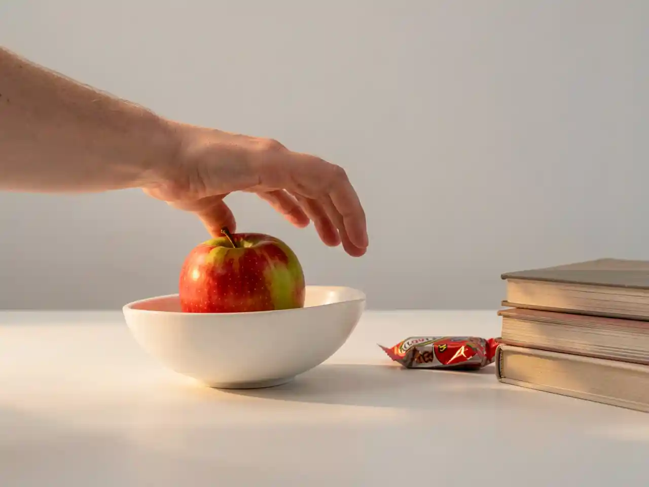 A hand reaching for a healthy apple placed prominently, while a candy bar is slightly out of reach, symbolizing how environment shapes better choices.