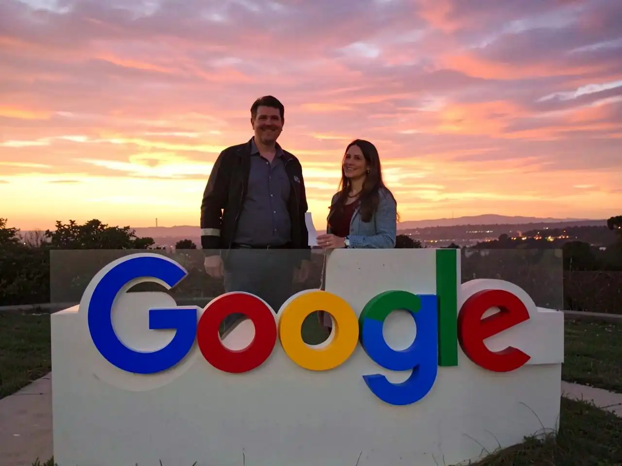 man and woman standing behind google logo with sunset background