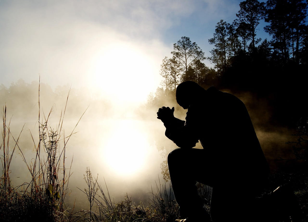 A silhouette of a person kneeling in prayer at dawn's light