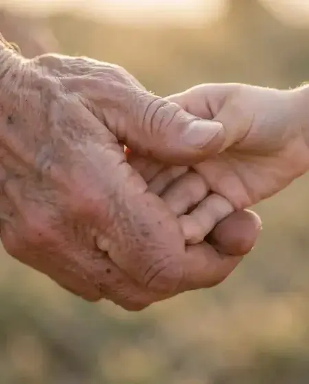 Close-up of an elder's weathered hand gently holding a child's small hand, bathed in warm sunlight, symbolizing the enduring human longing for kindness and connection
