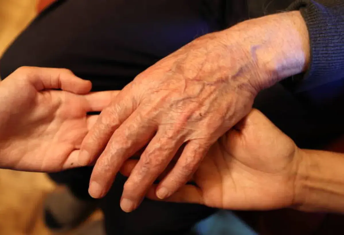 A young person holding an elder’s hand symbolizing care and respect.