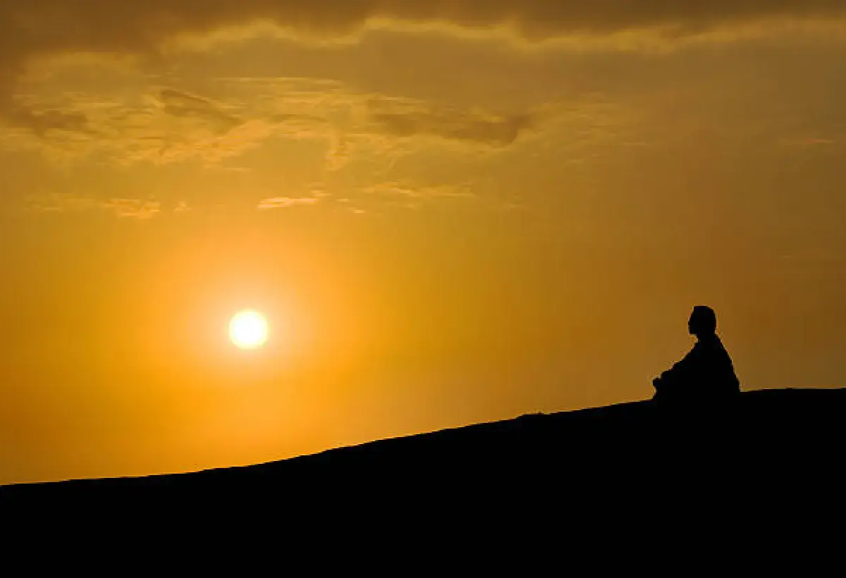 A person reflecting on a hilltop at sunset, overlooking a vast horizon