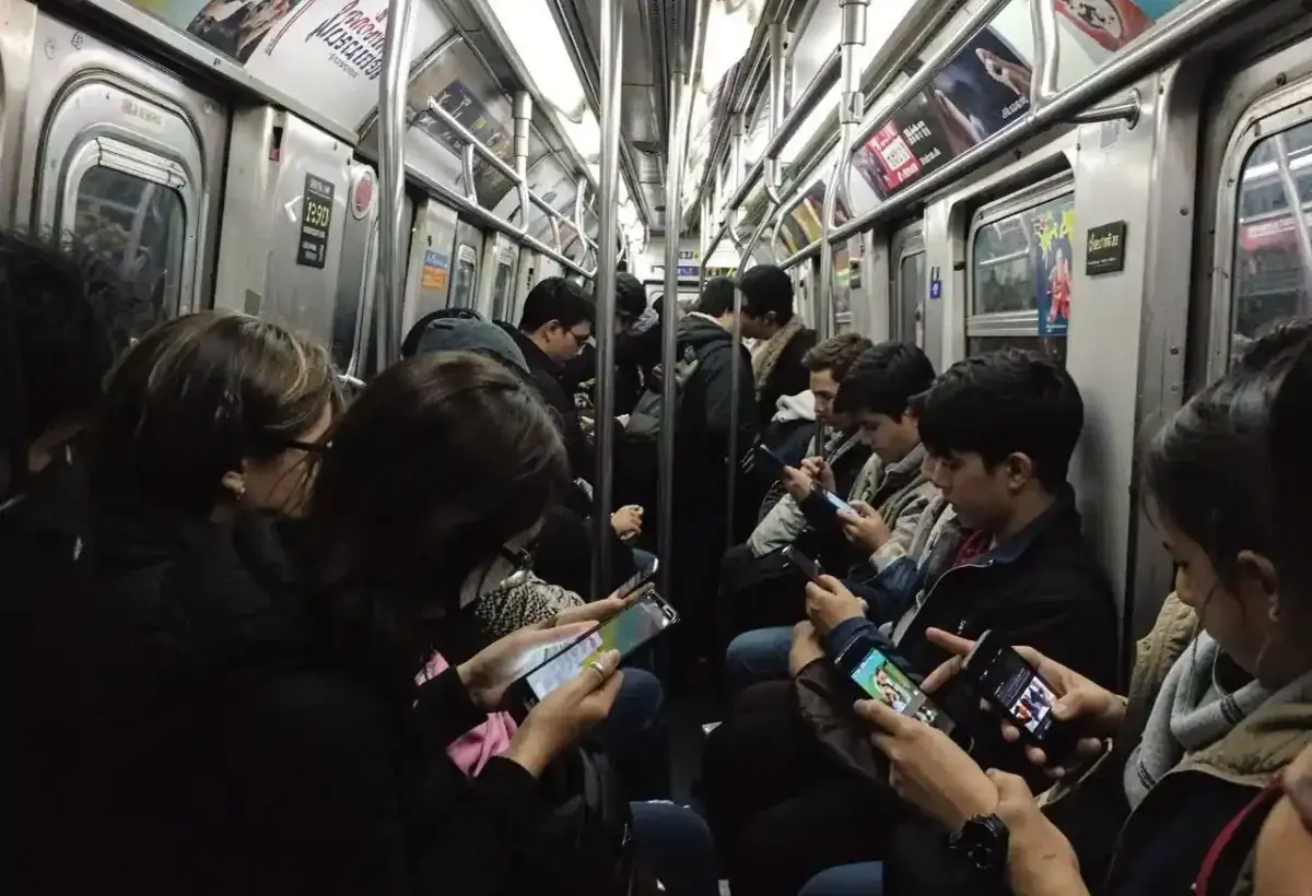 Busy subway train where several passengers without earphones are using phones with different media playing.