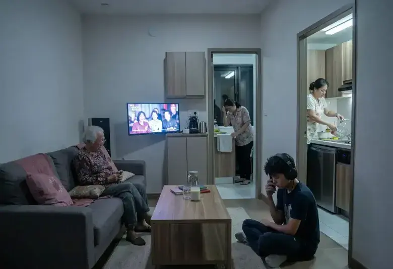 Three generations of a Filipino family in a cramped condo living room, each isolated by screens and tasks, symbolizing the emotional strain behind multigenerational living