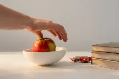 A hand reaching for a healthy apple placed prominently, while a candy bar is slightly out of reach, symbolizing how environment shapes better choices.