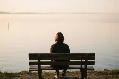 A person sitting alone on a bench overlooking a calm lake at sunset, symbolizing quiet reflection, inner peace, and the journey of self-discovery
