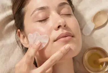 Close-up of a person's calm face with a hand gently gliding a rose quartz Gua Sha tool along the jawline, representing the science-backed practice of facial yoga and Gua Sha for non-invasive skin lifting