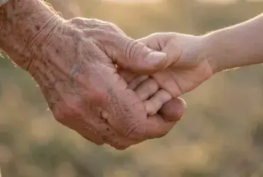 Close-up of an elder's weathered hand gently holding a child's small hand, bathed in warm sunlight, symbolizing the enduring human longing for kindness and connection