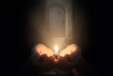 Cupped human hands gently holding a single, tiny glowing flame, whose light softly expands to illuminate a faint path in the surrounding darkness, symbolizing the quiet power of a willing heart and the divine multiplication of even the smallest faith