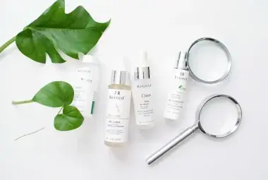 Flatlay of retinol skincare products with a magnifying glass and green leaf
