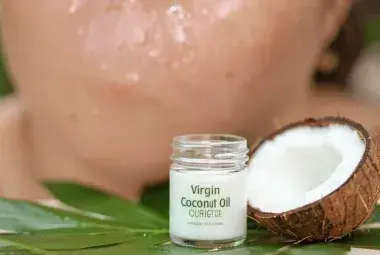 Glass jar of virgin coconut oil with green leaf, woman's glowing skin in background