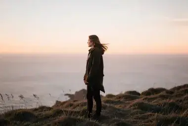 Lone figure standing on a windswept hill at dusk, contemplating in the quiet light