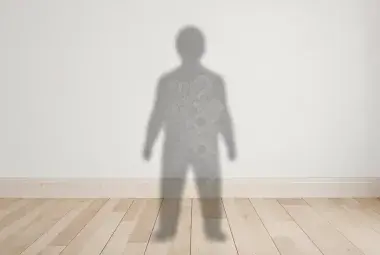 Minimalist image of a person's shadow on a wall filled with faint outlines of question marks, tangled threads, and chains, symbolizing invisible mental and emotional clutter