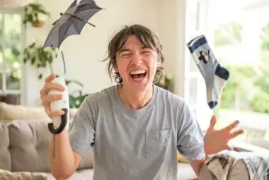 Person laughing while juggling an umbrella, coffee cup, and mismatched sock