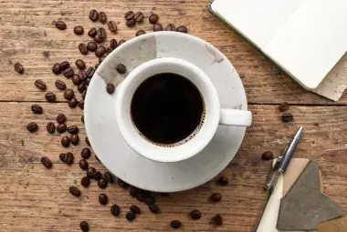 Top-down view of a coffee cup with steam, surrounded by scattered coffee beans on a wooden table
