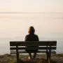 A person sitting alone on a bench overlooking a calm lake at sunset, symbolizing quiet reflection, inner peace, and the journey of self-discovery