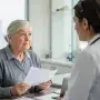 Older patient thoughtfully listening to a doctor, representing the balance between trust and personal agency in aging