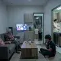 Three generations of a Filipino family in a cramped condo living room, each isolated by screens and tasks, symbolizing the emotional strain behind multigenerational living